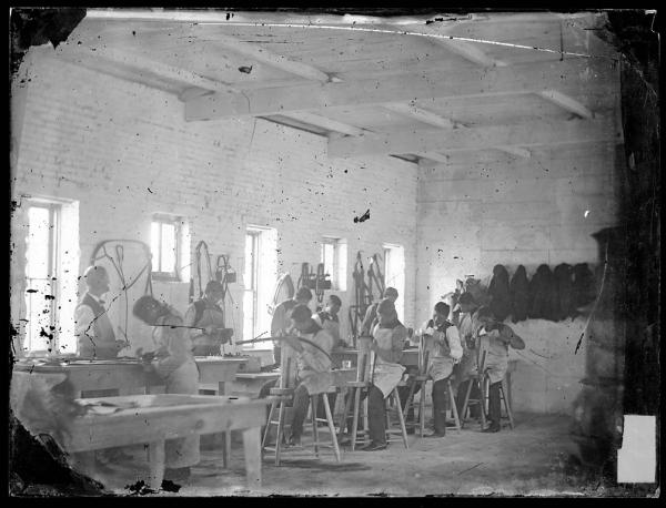 Instructor and students in the harness making shop, c.1882