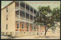 color image; view of corner of the building of large boys' quarters, the building has three levels and porches running across the front of the building, in has been recolored red (like brick) in front, a tree sits in front of the building to the right