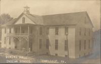 sepia-toned view of the dining hall from the perspective of the girls' quarters, there is a telephone or telegraph pole in front of the building (on the right side), a small group of young women stand on the porch