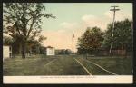 A postcard with an image of the school campus, tennis courts are in the foreground and a tree, gymnasium, and telephone wires are in the background