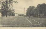 black and white image; view of campus from perspective of the academic buildings, in the center of the background is the flagpole, fire hydrant in middle ground, painted lines of the tennis courts are in the foreground