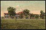 color image; view of the academic building (two story building with central area and two wings), building has been painted red in post-production, there are trees, a path, lines for a tennis court, and fire hydrant in front of the building