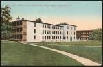 color image; view of the girls' quarters and gymnasium taken from perspective of the superintendent's quarters (both buildings have three stories, white walls, flat roofs), large boys' quarters is in the background