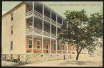 color image; view of corner of the building of large boys' quarters, the building has three levels and porches running across the front of the building, in has been recolored red (like brick) in front, a tree sits in front of the building to the right