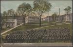 color image; students assembled in formation in the foreground, with the camera facing east viewing the whole length of the campus, the students are in black and white, there are leaves on the trees, the sky is orange near the horizon and blue above that