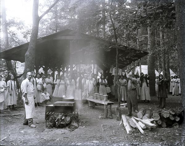 Female students posed behind outdoor cooking grill at Camp Sells, c. 1913