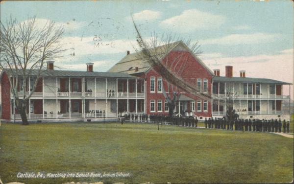 color image; view of the academic building with a group of students lined up along the path leading to the building, center part of the building has been painted red (like brick)