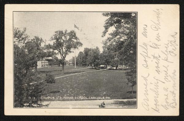 black and white image; view of central campus taken from a slight height, most buildings are obscured by trees but you can see the flag pole, a little bit about of the administration building and large boys' quarters
