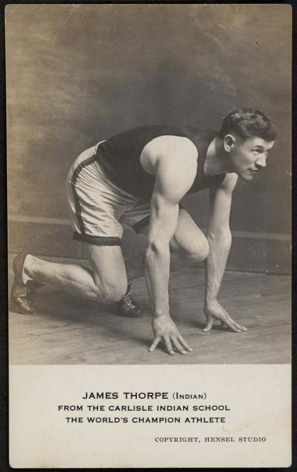 black and white image; portrait of Jim Thorpe in athletic clothings, he is posed as if he about to start sprinting and he is looking to the right