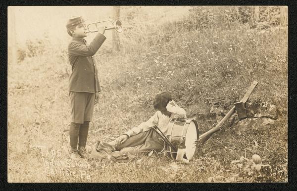 Sepia toned image, two young boys are on a grassy hill, one stands (possibliy in school uniform) and plays a bugle, the other boy sits in the grass and leans on a drum