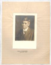 photograph of man looking to the right, wears suit and tie, short dark hair