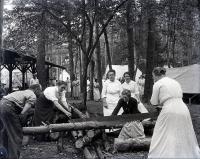 Female staff sawing a log at Camp Sells, c. 1913