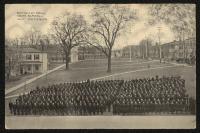 black and white image; large group of students (possibly entire school) lined up in tight rows in the foreground, photograph is taken from perspective of the academic building looking north-east