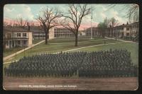 color image; view of the school grounds from perspective of the academic building towards the quarters, the trees have no leaves, in the foreground is a set of students arranged in tight rows (they are in color), the sky closest to the horizon has been painted pink, the rest is blue with faint clouds