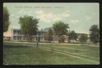color image; view of the front of the academic building, the center of the building has been colored brown, trees stand in front of the building, a fire hydrant is in the foreground
