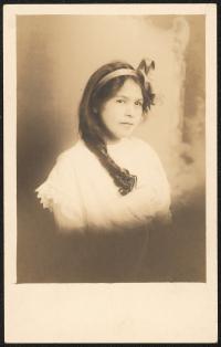 sepia-toned image; portrait of young woman (head to mid-torso), she is wearing a white top, her hair is gathered in one piece over her right shoulder and a ribbon bow is tied on the crown of her head