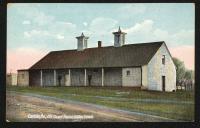 color image; view of guard house, in foreground is a road, there are two men standing on the porch of the building, the sky near the horizon is pink and the rest is blue; reproduction (with cropping) of photograph circa 1899
