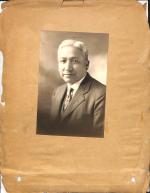 black and white photograph of a man in a suit and tie, smiling slightly