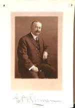 photograph of man in suit and tie, sitting sideways on chair
