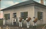 color image; six young men (probably students) stand outside building with Bakery sign, three carry loaves of bread