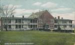 color image; view of the academic building with a group of students lined up along the path leading to the building, center part of the building has been painted red (like brick)