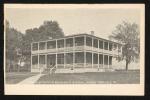 Administration Building Postcard black and white image; a view of the adminsitration building with the Superintendent's Quarters just barely visible along the left side, building is two stories tall with a wrap-around porch on each level with white railings