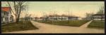 color image; postcard double in length of a normal postcard, photograph taken from the perspective of the guard house with the academic building on the far left and the quarters and gymnasium on the right