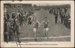 black and white image; photograph of the finish line of a track event, four young men are running towards the camera, the two in the front have a large M visible on their tops, a crowd of spectators stands on either side of the path to the finish line
