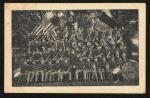 black and white image; photograph of the Carlisle Indian School band, fifty people sat on four levels of risers hold instruments, a bass drum with the words "Carlisle Indian School U. S." painted on it is visible in the right corner; 
