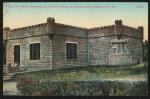 color image; view of the side of the art studio building, the entrance is just visible on the far left and there is hedgerow and a bit of road in the foreground