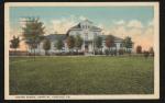 color image; view of the front of the hospital building, eight or nine small trees (with leaves) stand in front of it, the sky is orange along the horizon then blue up above