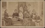 Eight female students on the steps of the Girls' Quarters with teacher, c.1885