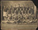 Track Team sepia toned photograph of 22 men sitting and standing in rows, all except Glenn Warner wear a dark shirt and light shorts with track shoes, two hold rabbits