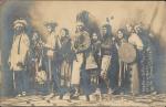 Nez Perce Students (pose 2) real photo postcard; group portrait of nine people standing in a row wearing regalia, two hold shields