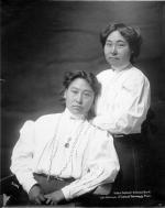 black and white photo of two Alaskan women, one seated at left and one standing at right
