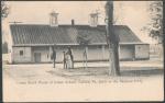 black and white image; guard house (single story building with a porch and two cupolas) pictured with two men and a boy in the foreground